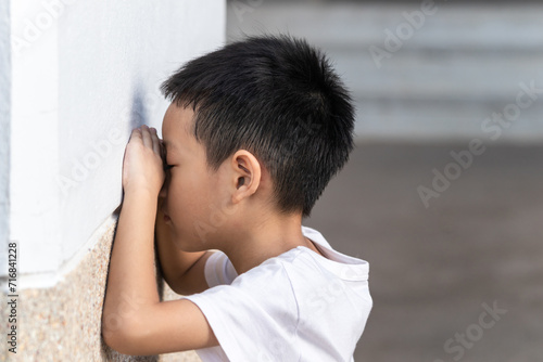 The cute Asian little boy is playing hide and seek with the funny moments. Asian kid crying on the wall. Child playing hide-and-seek hiding face.