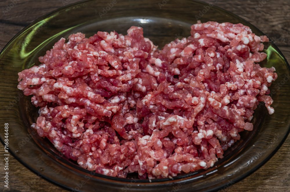 Minced meat in a plate on a wooden table, top view