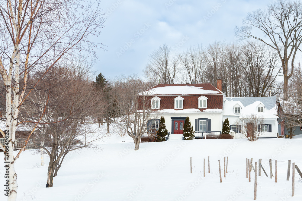 Selective focus view of beautiful French-style patrimonial white double house with shingles and metal roof in a snowy land, Neuville, Quebec, Canada