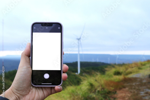 Woman holding mobile phone with blank screen while, With of windmill landscape view. Clean energy concept, wind power