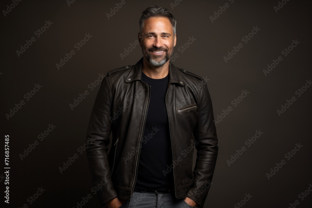 Portrait of a blissful man in his 40s sporting a classic leather jacket against a blank studio backdrop. AI Generation