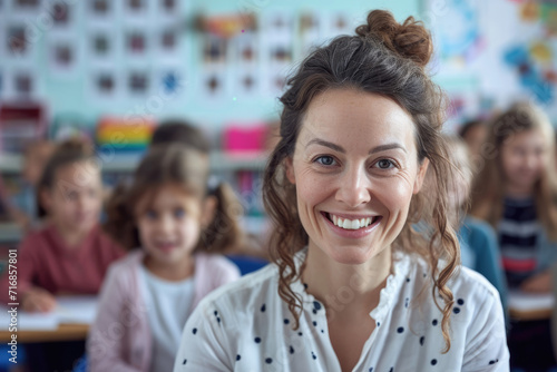Portrait of smiling beautiful teacher in a class at elementary school looking at camera with students on background