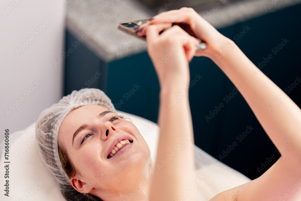 Naklejka premium a girl lies on sofa in beauty salon taking a photo of her face with gel during a cosmetic procedure