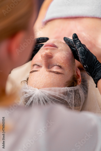 close-up beautician in gloves rubs the serum with massage movements on the face of a client in salon