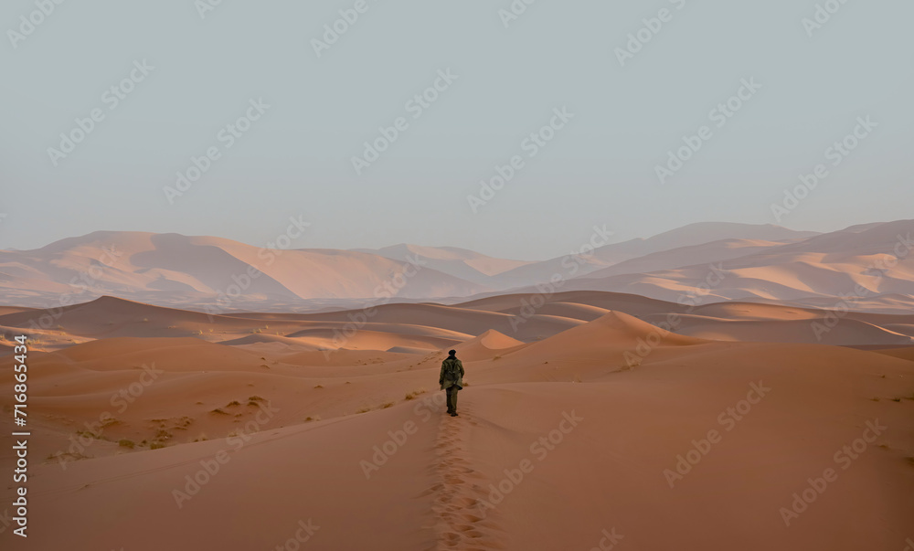 Lone anonymous traveler trekking across the Merzouga Desert in Morocco Lone anonymous traveler trekking across the Merzouga Desert in Morocco