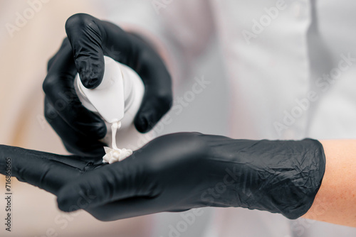 close-up beautician in gloves squeezes cleansing gel or foam on hand for beauty treatment