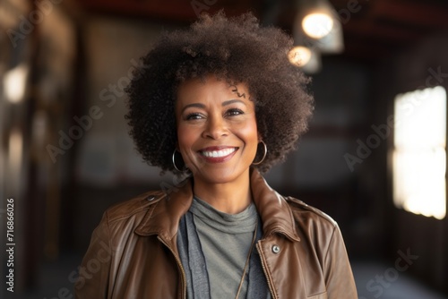 Portrait of a grinning afro-american woman in her 60s wearing a trendy bomber jacket against a empty modern loft background. AI Generation