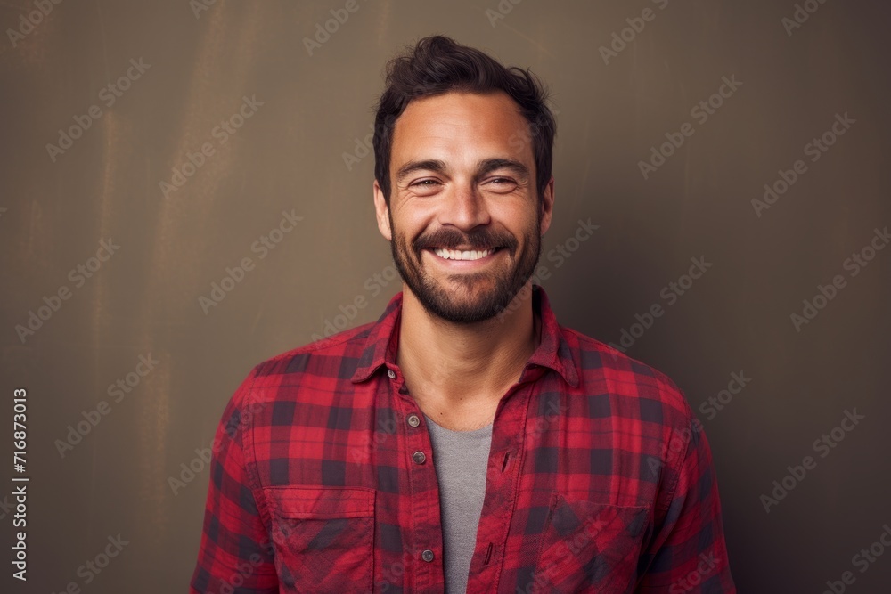 Obraz premium Portrait of a smiling man in his 30s dressed in a relaxed flannel shirt against a plain cyclorama studio wall. AI Generation