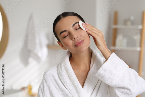 Beautiful woman removing makeup with cotton pad in bathroom  space for text