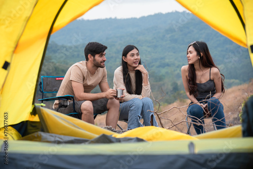 Group of three people sitting outside the yellow tent having fun conversation, friends are engaged sitting relaxation free time after hiking outdoors activities fall season, tourist friends traveling