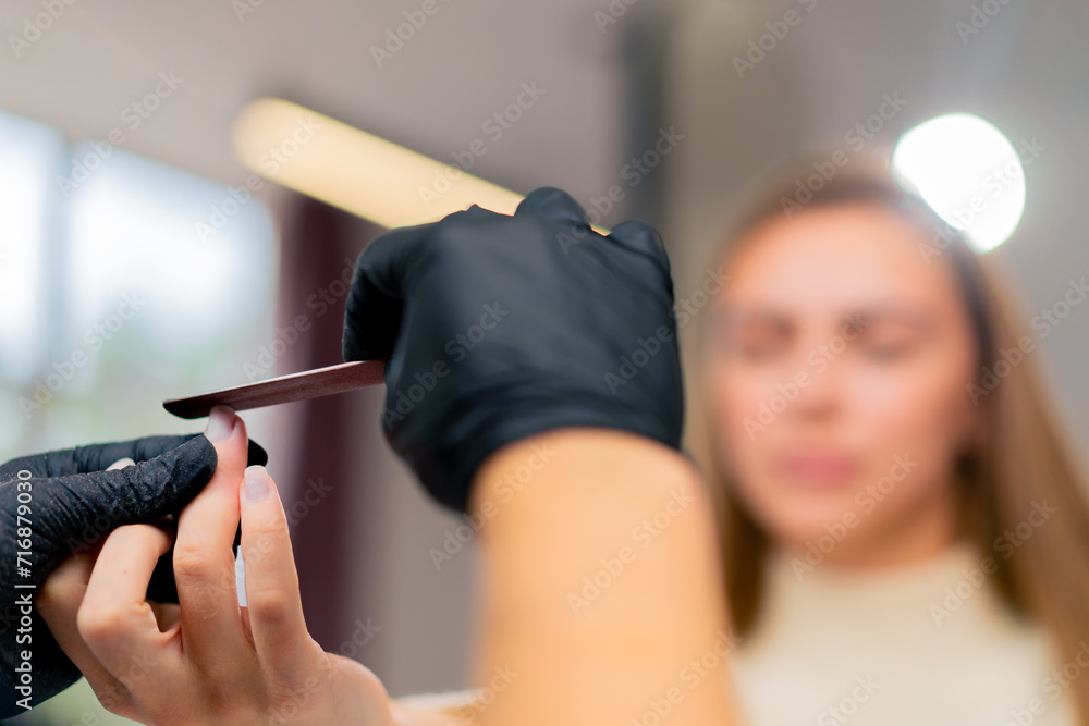 close-up of a manicurist cutting out the shape of a girl's nails with a file a care procedure
