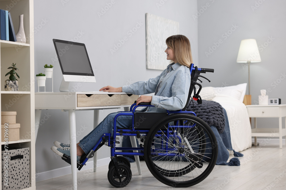 Woman in wheelchair using computer at table in home office Woman in wheelchair using computer at table in home office