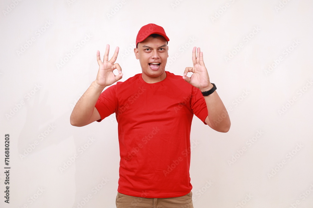 Handsome young asian courier standing while showing okay hands gesture against white background