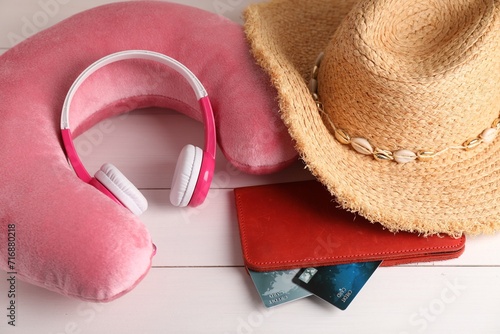 Pink travel pillow, hat, headphones and wallet with credit cards on white wooden background, above view photo