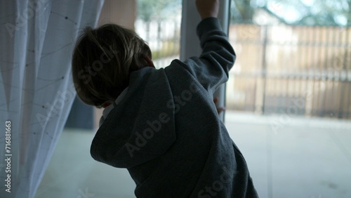 Back of child closing apartment door behind him, overview of terrace in background, closes doorknob tight