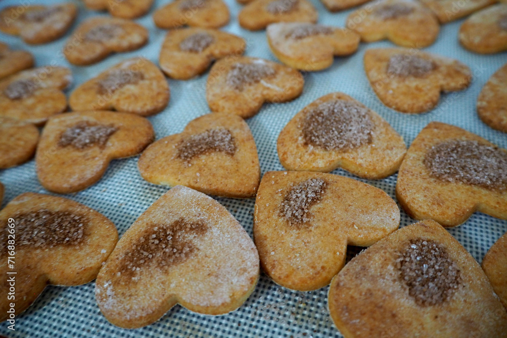 On a silicone mat there are a lot of gluten-free cottage cheese cookies in the shape of hearts sprinkled with cinnamon and sugar after baking in the oven