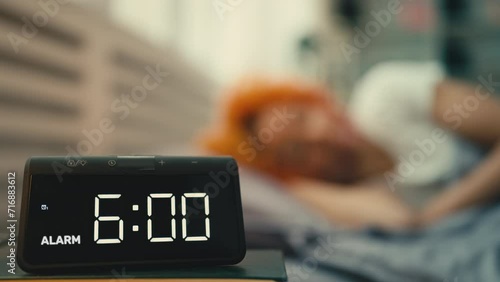 Young woman wakes up at six o'clock in the morning and turns the alarm clock off photo