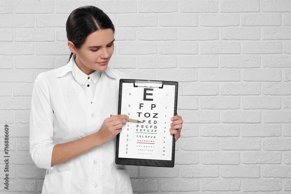 Ophthalmologist pointing at vision test chart near white brick wall, space for text