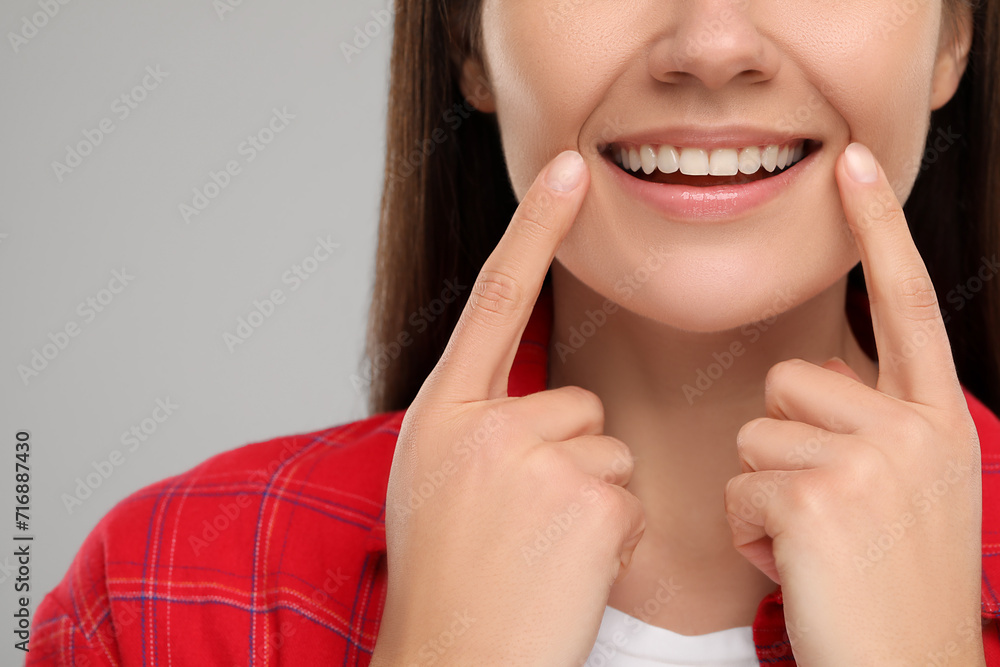 Woman showing her clean teeth and smiling on light grey background, closeup Woman showing her clean teeth and smiling on light grey background, closeup