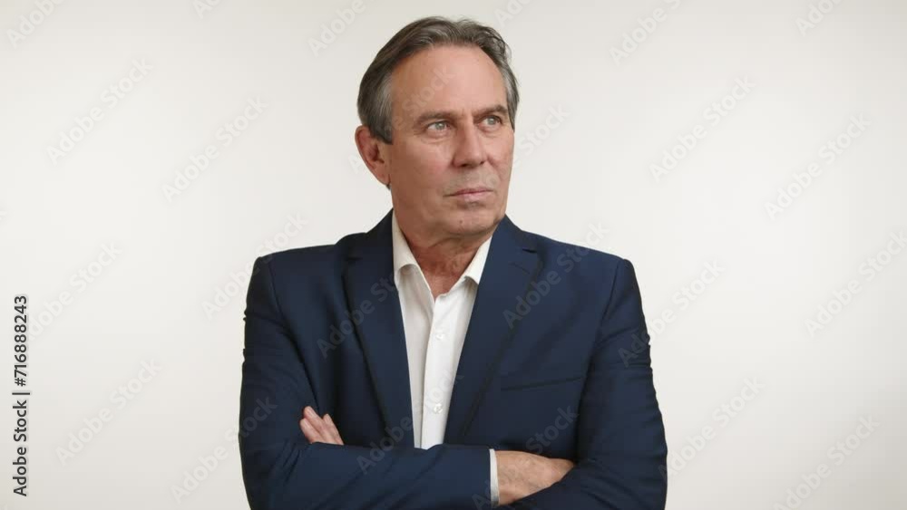 A discerning senior businessman in a navy suit stands arms crossed ...