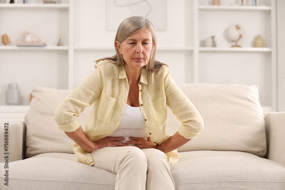 Menopause. Woman suffering from abdominal pain on sofa at home Menopause. Woman suffering from abdominal pain on sofa at home
