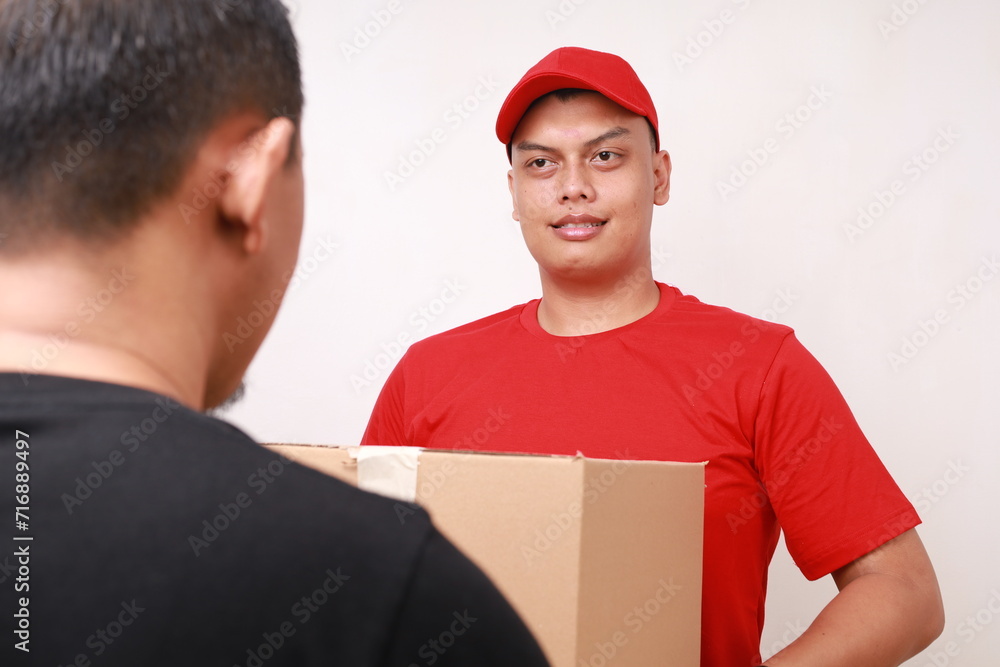 Asian courier man in red delivering cardboard box parcel to person. Isolated on white Asian courier man in red delivering cardboard box parcel to person. Isolated on white
