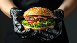 A cook in black gloves holds a huge, beautiful, juicy and appetizing cheeseburger. Sesame bun. Cooking hamburger, fast food in a restaurant.