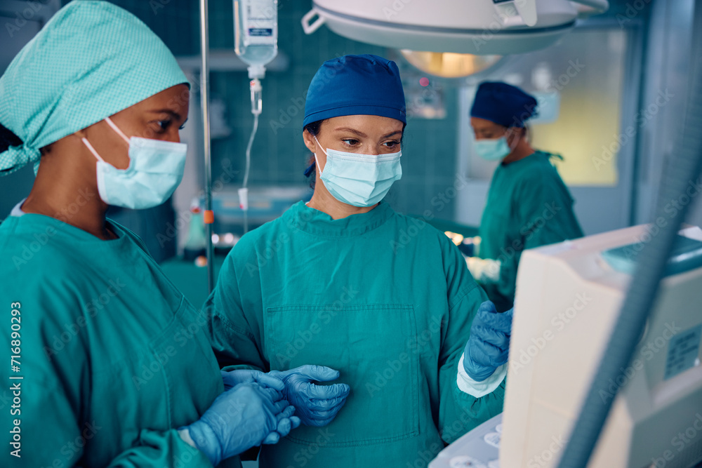 Female surgeons cooperating while looking at patient's vitals on monitor in operating room. Female surgeons cooperating while looking at patient's vitals on monitor in operating room.
