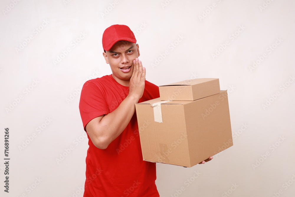 Asian courier man in red whispering while holding a cardboard box. Isolated on white Asian courier man in red whispering while holding a cardboard box. Isolated on white