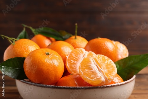 Fresh tangerines with green leaves in bowl on wooden table, closeup