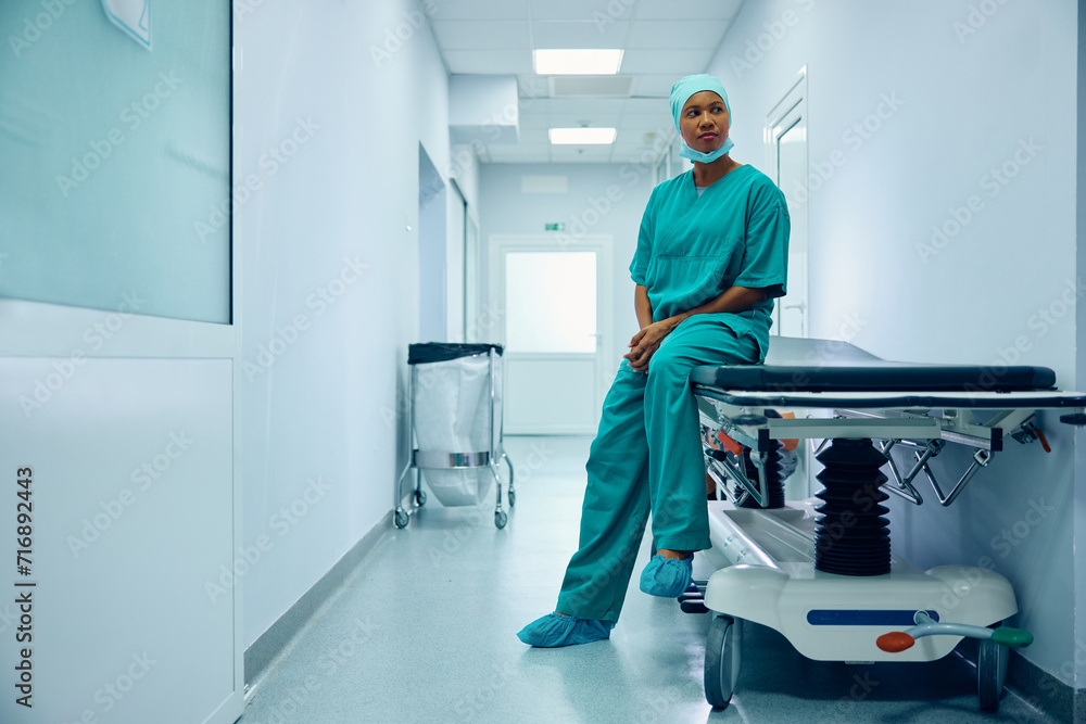 Pensive black female surgeon on break in hospital hallway. Pensive black female surgeon on break in hospital hallway.