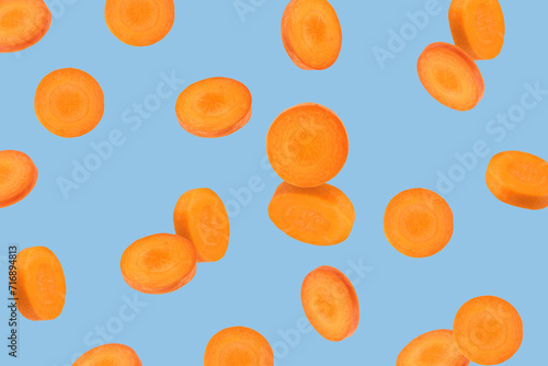 Fresh carrot slices falling on light blue background