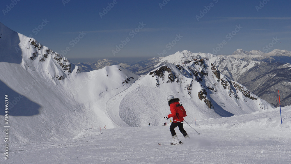 Skier skiing down snowy slope in mountains at ski resort. Adrenaline in blood from speed and breathtaking mountain scenery with snow capped peaks and glaciers. Winter recreation and sports. In motion