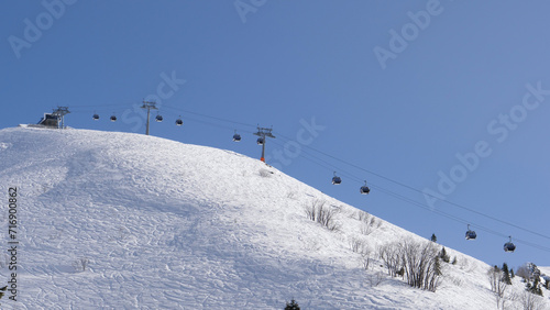 Ski resort on sunny winter day. Ski lift funicular cab lifts skiers and snowboarders up mountain against clear blue sky. Breathtaking view of snowy mountains resort and valleys of glaciers.