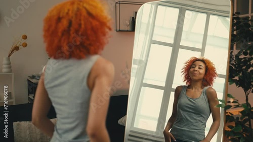 Young African American woman using perfumed deodorant in front of mirror, care photo