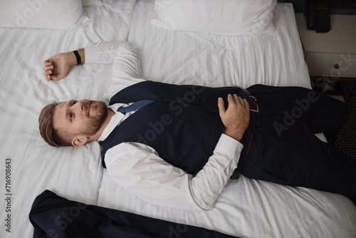 High angle portrait of smiling young businessman falling into hotel bed after long travel