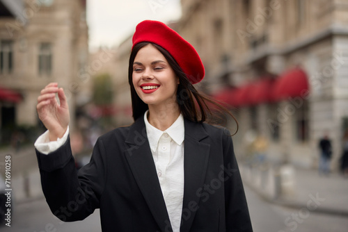 Fashion woman portrait smile with teeth standing on the street in front of the city tourist in stylish clothes with red lips and red beret, travel, cinematic color, retro vintage style, urban fashion.