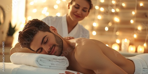 Attractive male receiving rejuvenating back treatment at spa, unwinding in tranquil setting and reenergizing after a busy day, with therapist administering healing back rub to promote healthy living. photo