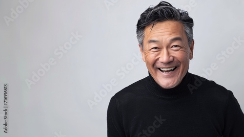 Middle-aged Asian gentleman in a dark sweater grinning joyfully while glancing towards the lens. photo