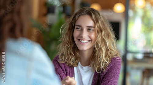 Young woman with curly hair smiling warmly, seemingly engaged in a happy and casual conversation with someone out of frame.