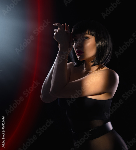 Portrait of a beautiful brunette dancer girl with a French bob hairstyle on a stage with red light effects in the dark. Beauty close-up portrait.