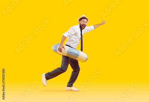 Side profile view funny happy joyful excited man office worker in white shirt, black tie, trousers, sun hat and beach ring running isolated on yellow color background. Summer holiday, vacation concept