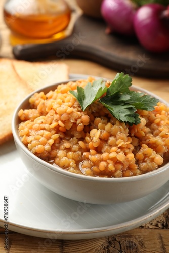 Delicious red lentils with parsley in bowl served on table, closeup