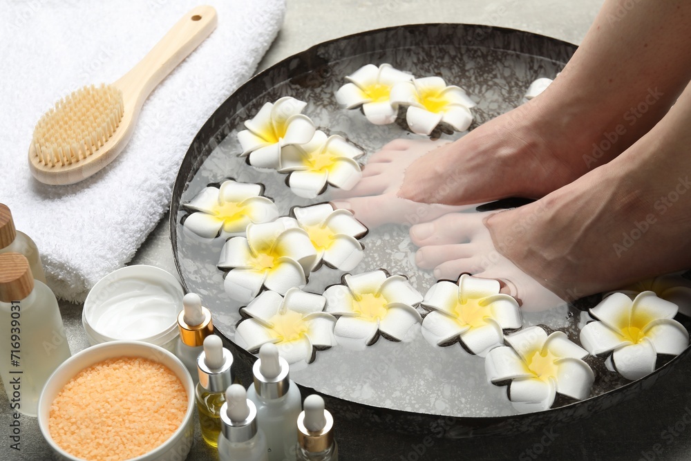 Woman soaking her feet in bowl with water and flowers on floor, closeup. Spa treatment Woman soaking her feet in bowl with water and flowers on floor, closeup. Spa treatment