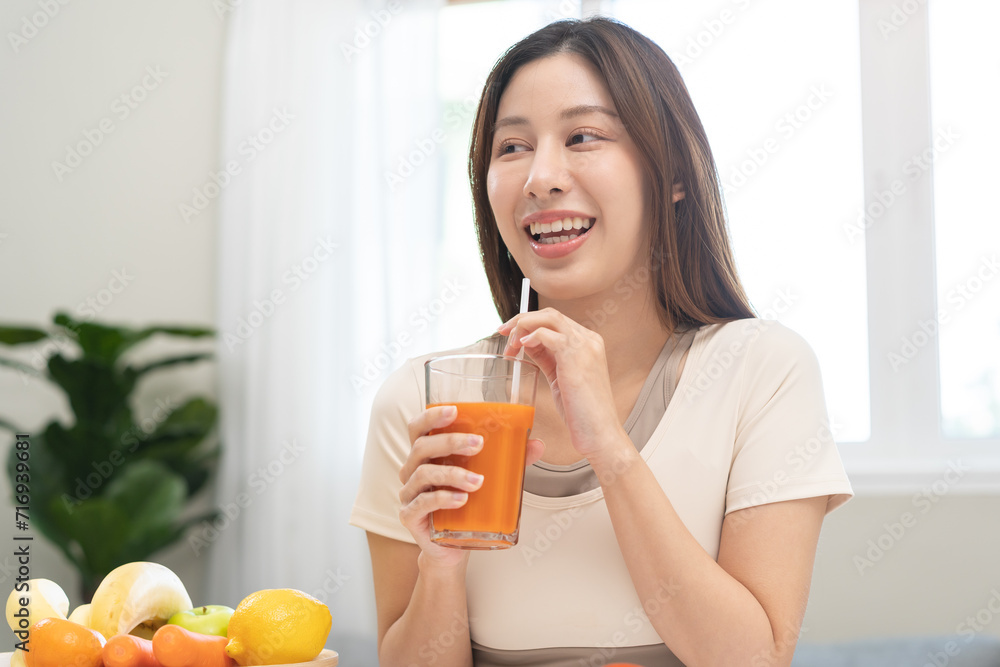 Orange detox juice concept, smile asian young woman hand holding a glass of vegetable juice, carrot smoothie for diet at home, drinking healthy meal food for weight loss. Lifestyle, vegan nutrition. Orange detox juice concept, smile asian young woman hand holding a glass of vegetable juice, carrot smoothie for diet at home, drinking healthy meal food for weight loss. Lifestyle, vegan nutrition.