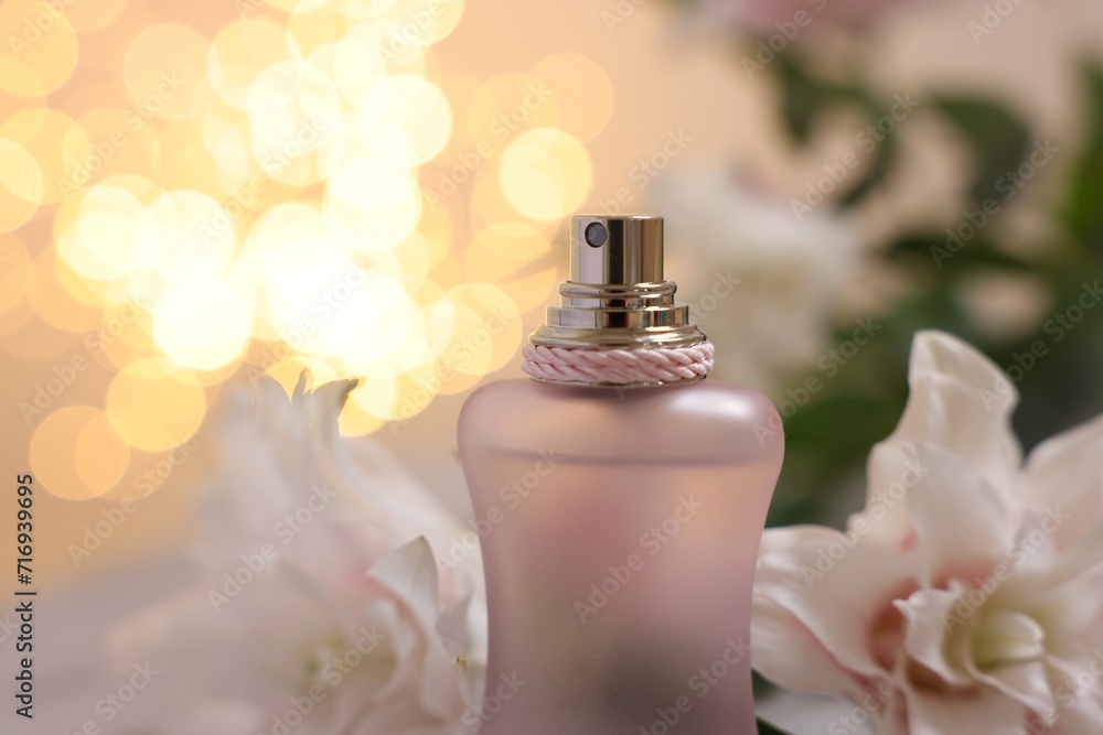 Bottle of perfume and beautiful lily flowers against beige background with blurred lights, closeup Bottle of perfume and beautiful lily flowers against beige background with blurred lights, closeup