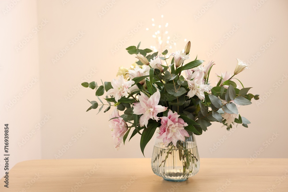 Bouquet of beautiful lily flowers in vase on wooden table against beige background Bouquet of beautiful lily flowers in vase on wooden table against beige background