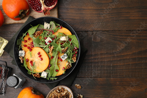 Tasty salad with persimmon, blue cheese, pomegranate and walnuts served on wooden table, flat lay. Space for text