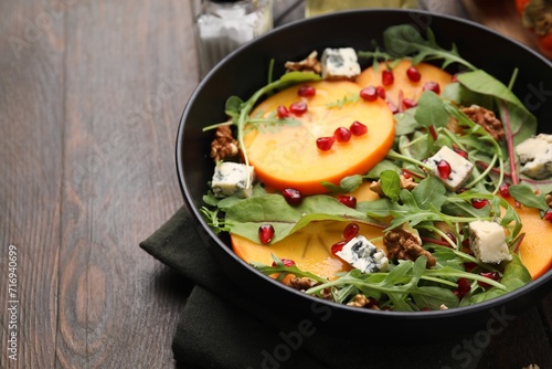 Tasty salad with persimmon, blue cheese, pomegranate and walnuts served on wooden table, closeup. Space for text