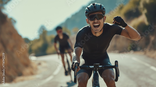 cyclist is celebrating enthusiastically with a raised fist while riding on a road, with another cyclist trailing behind